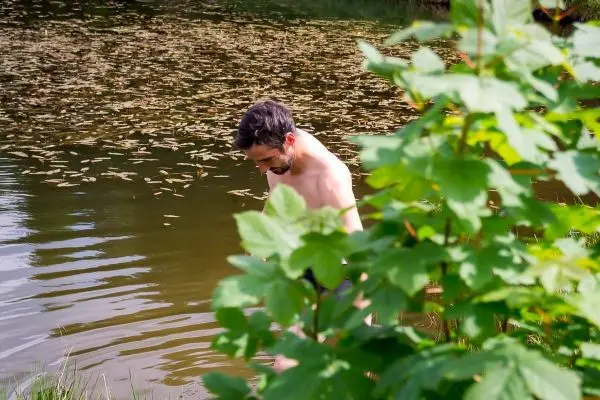 Mann steht am Ufer eines Gewässers und beugt sich nach vorne