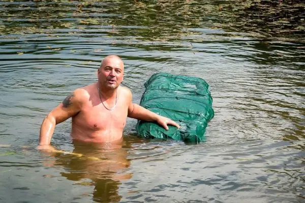 Mann steht im Wasser und hält eine grüne, verpackte Struktur