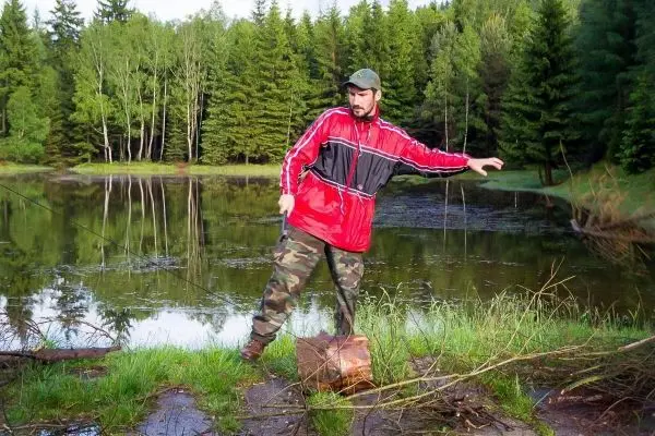 Mann zieht mit einer Schnur an einem Holzstück am Ufer eines Gewässers