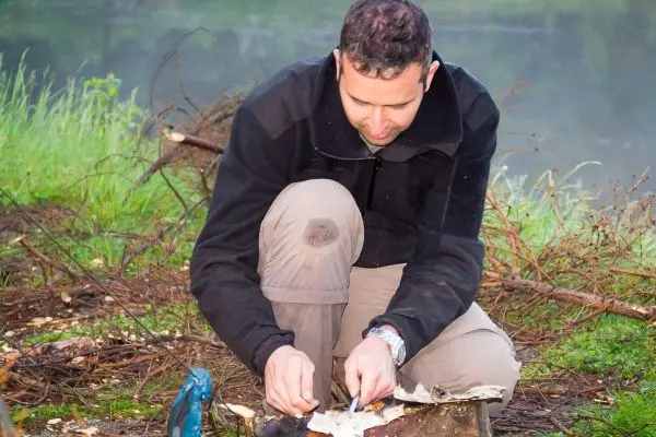 Mann zündet Zunder mit Feuerstahl und Funken auf Holzstück