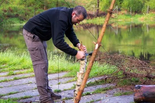 Messer bearbeitet einen Holzstock am Ufer eines Gewässers