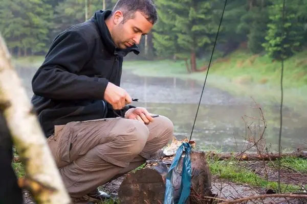 Messer bearbeitet Holzstück zur Vorbereitung von Zunder am Ufer eines Gewässers