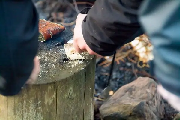 Messer schabt Zunder von einem Holzstück auf einem Baumstumpf