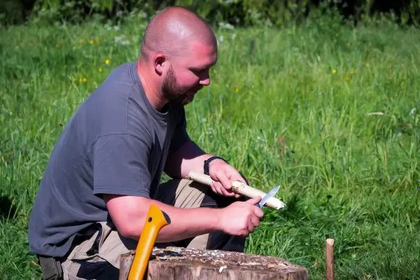 Messer schnitzt Holzstück auf einem Baumstumpf im Freien