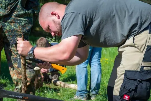 Person bearbeitet einen Stock mit einer Säge beim Überlebenstraining