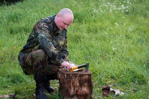 Person bearbeitet Holz mit einer Axt auf einem Baumstumpf
