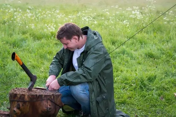 Person bearbeitet Holz mit einer Axt auf einem Baumstumpf
