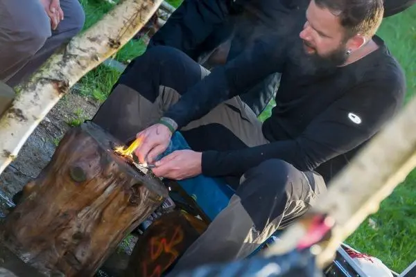 Person entzündet Feuer auf einem Holzstamm beim Survival Training