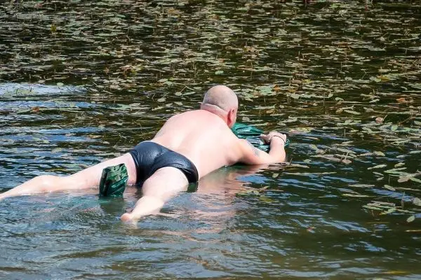 Person liegt auf dem Bauch im Wasser und greift nach etwas
