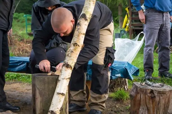 Person schnitzt mit einem Messer an einem Holzblock beim Überlebenstraining