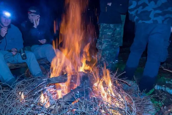 Person sitzt am Feuer und hält eine Taschenlampe in der Hand