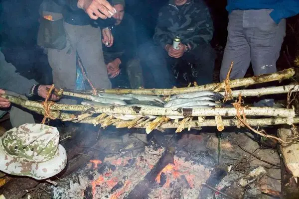 Personen halten eine selbstgebaute Grillvorrichtung über dem Feuer