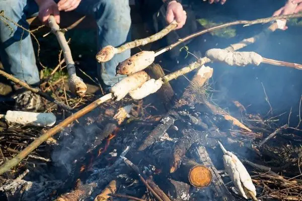 Stöcke mit Teig über einem offenen Feuer geröstet, Rauch steigt auf