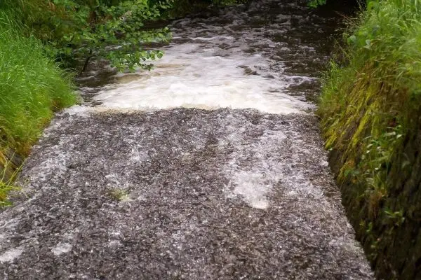 Wasser fließt über eine steinerne Rampe in einen kleinen Bach