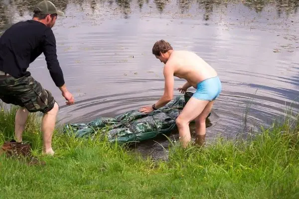 Zwei Personen heben eine camouflagefarbene Ausrüstung aus einem Gewässer