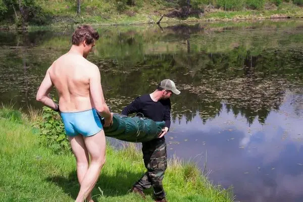 Zwei Personen heben eine grüne Tasche in der Nähe eines Gewässers