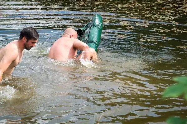 Zwei Personen im Wasser heben ein grünes Objekt