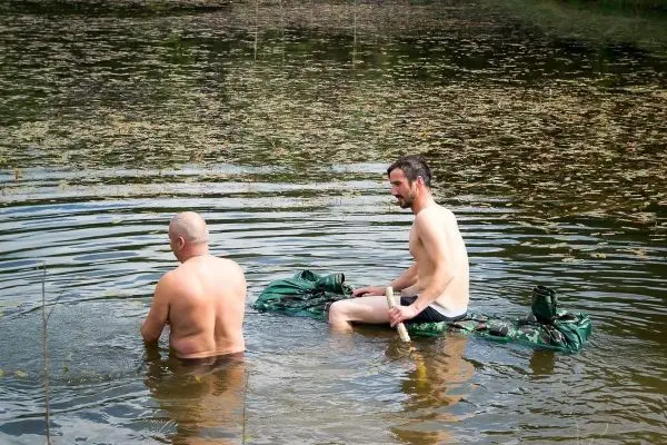 Zwei Personen sitzen im Wasser und halten sich an einem schwimmenden Untergrund fest