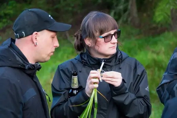 Zwei Personen stehen nebeneinander, eine hält eine Pflanze und ein Werkzeug