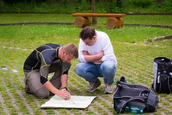 Zwei Personen studieren eine Karte auf dem Boden, eine Tasche liegt daneben