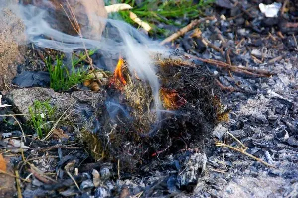 Brennendes Material mit Rauch und Glut auf dem Boden