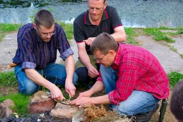 Drei Personen arbeiten gemeinsam an einem Feuerplatz mit Steinen und Zunder