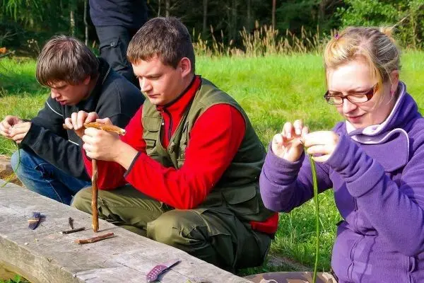 Drei Personen bearbeiten Holzstücke und Pflanzenmaterial auf einer Holzbank