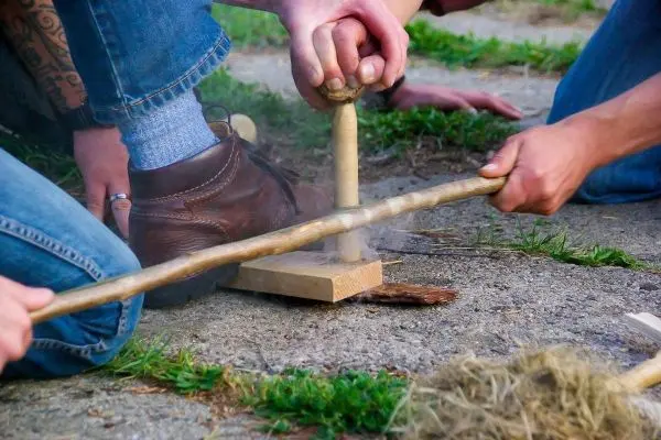 Feuerbohrer erzeugt Rauch durch Reibung auf Holzstück