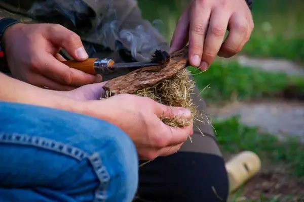 Feuerstahl erzeugt Funken auf Zunder in Händen, Rauch steigt auf