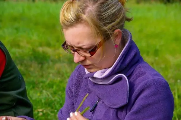 Frau hält zwei Grashalme in der Hand und schaut konzentriert darauf