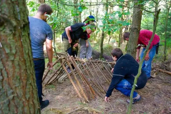 Gruppe baut eine selbstgebaute Konstruktion aus Ästen im Wald