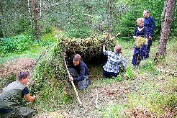 Gruppe baut eine Tarp-Notunterkunft aus Ästen und Gras im Wald