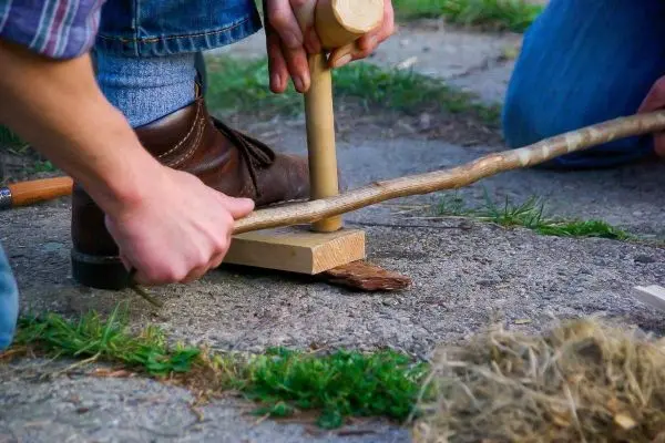 Holzstück wird mit einem Stock bearbeitet, um Feuer zu erzeugen