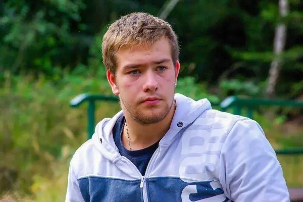 Junge sitzt im Freien, umgeben von Bäumen und Gras