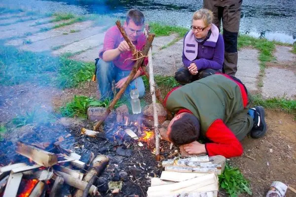 Kessel über Feuer mit Holzgestell, Person bereitet Zunder vor