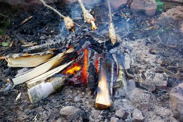 Kleine Flamme glimmt zwischen Holzscheiten im Feuerplatz