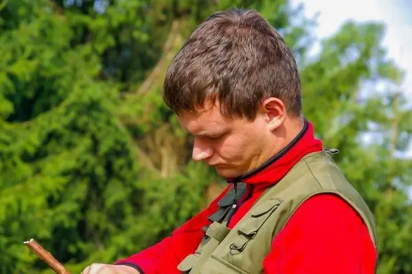 Mann bearbeitet einen Stock mit einem Messer im Freien