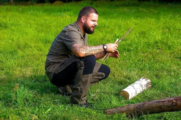 Mann kniet im Gras und hält zwei Äste in der Hand