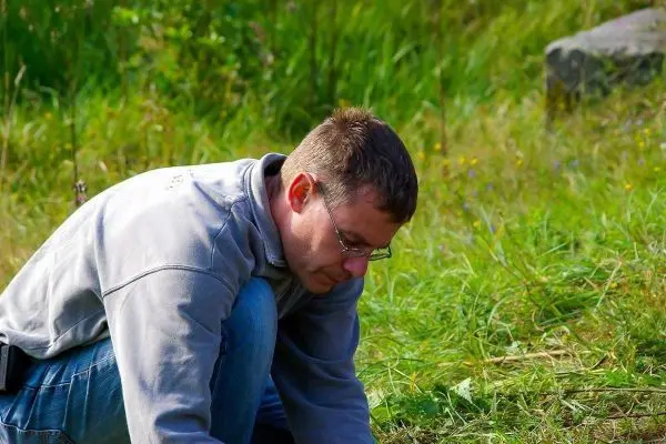 Mann kniet im Gras und untersucht den Boden