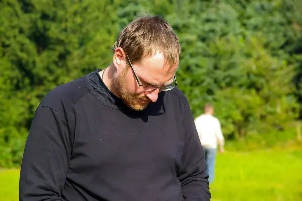 Mann mit Brille betrachtet Boden in einer grünen Umgebung