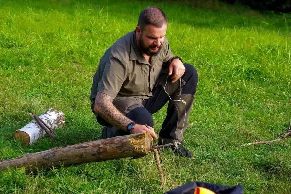 Person bearbeitet einen Holzstamm mit einer Schnur