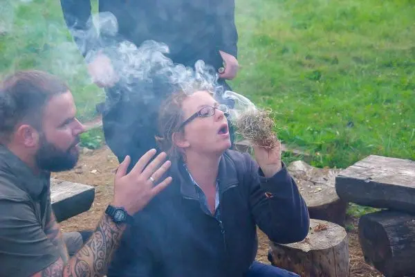 Person bläst Rauch aus einem Bündel Gras beim Feuer machen