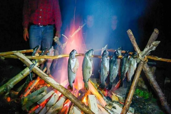 Person grillt Fische über einem Feuer beim Überlebenstraining