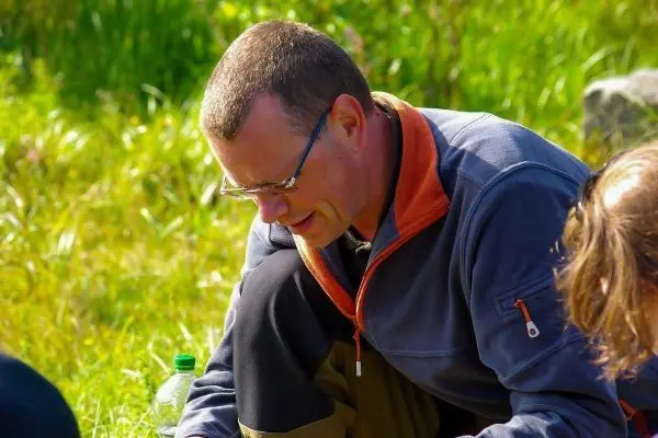 Person kniet auf dem Boden und betrachtet etwas im Gras