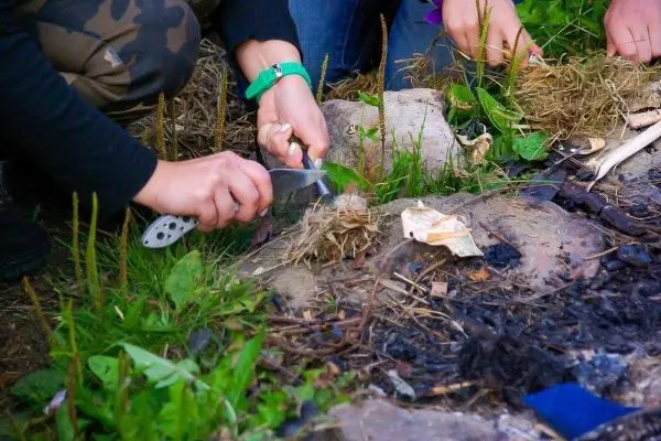 Person schneidet Material für Feuerstelle zurecht beim Survival Training