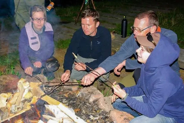 Personen rösten Zunder über einem kleinen Bodenfeuer mit langen Stöcken