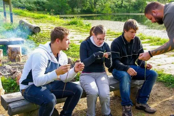 Vier Personen sitzen auf einer Bank und flechten mit Schnüren