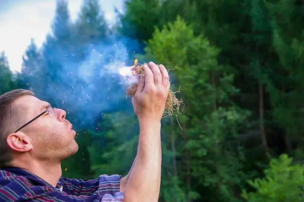 Zunder glimmt in der Hand, Rauch steigt auf