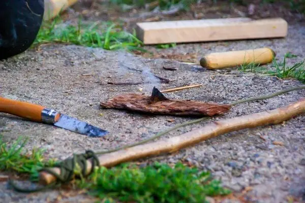 Zunder glimmt neben einem Messer und Holzstücken auf dem Boden