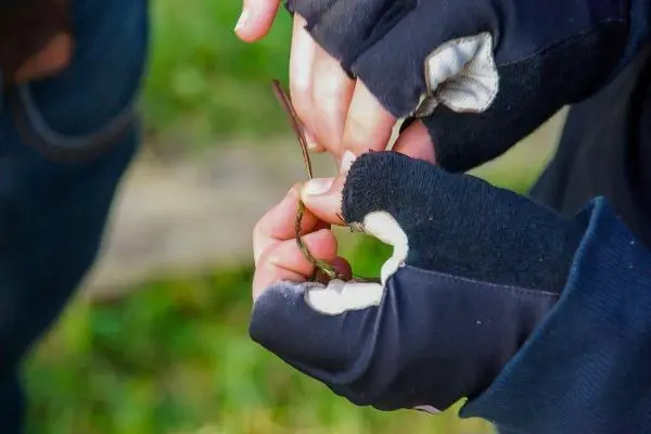 Zwei Hände knoten einen dünnen Ast mit Handschuhen